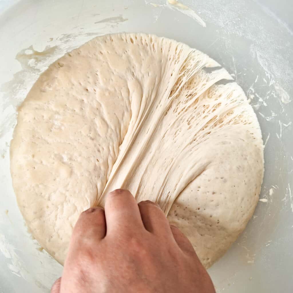 Hand pulling a proofed dough inside a large bowl