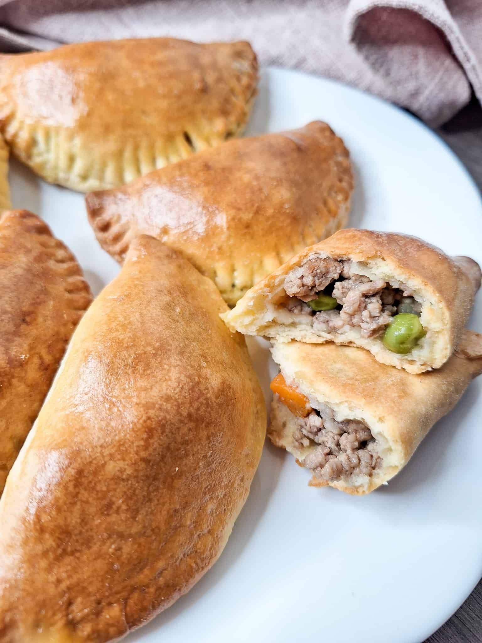 Closeup of the inside of baked Filipino meat empanadas next to other pieces on a white plate