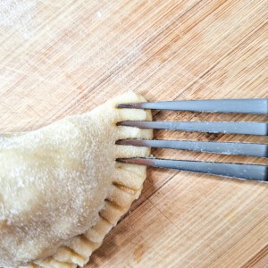 Crimping edges of empanada with the back of a fork