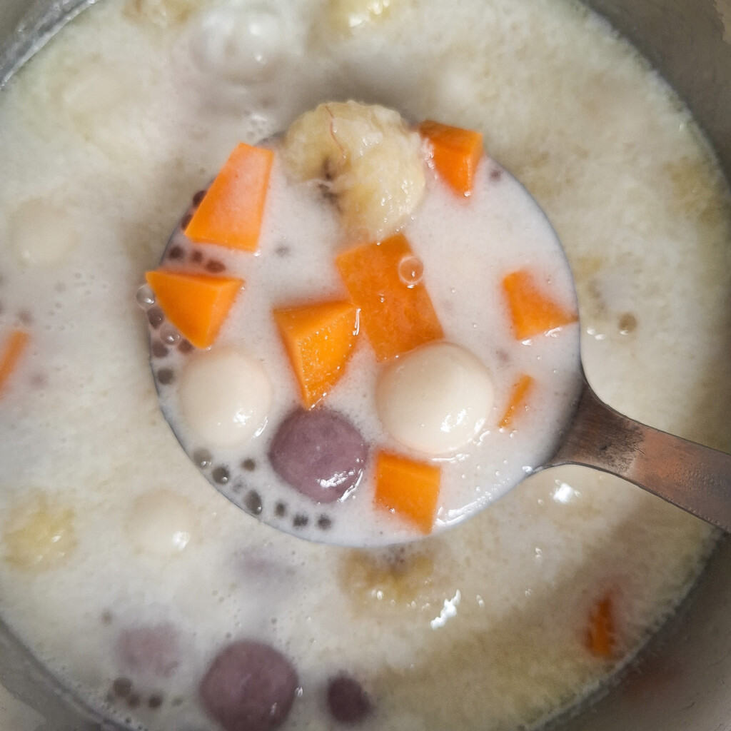 A pot filled with a coconut dessert soup, ladle showing sweet potatoes and glutinous rice balls