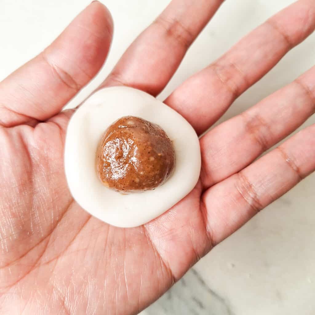 Hand holding a flattened rice ball with a caramel at the center of it.