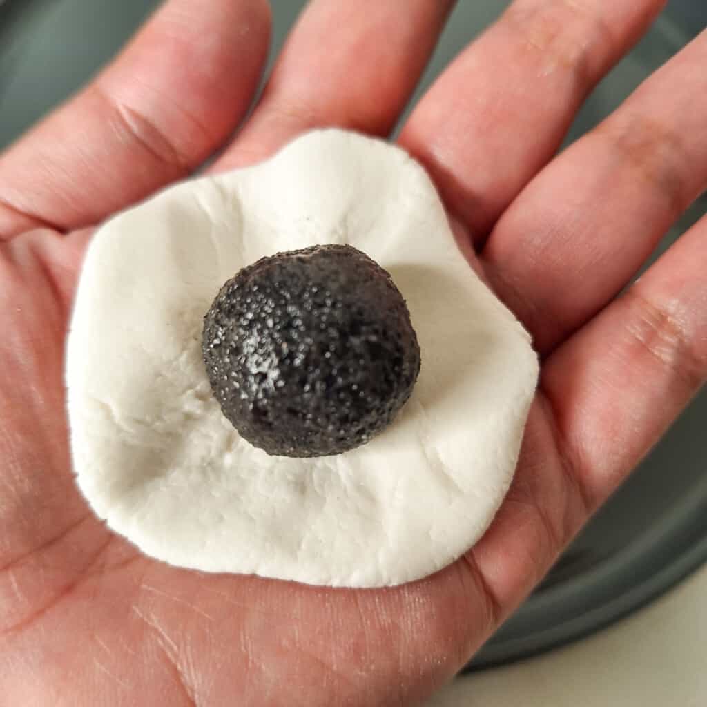 A piece of black sesame paste filling in the middle of a flattened dough